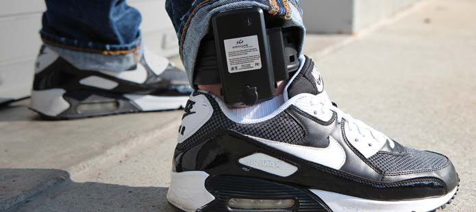 GPS ankle monitor device worn on a person's ankle over sneakers showing real-world size